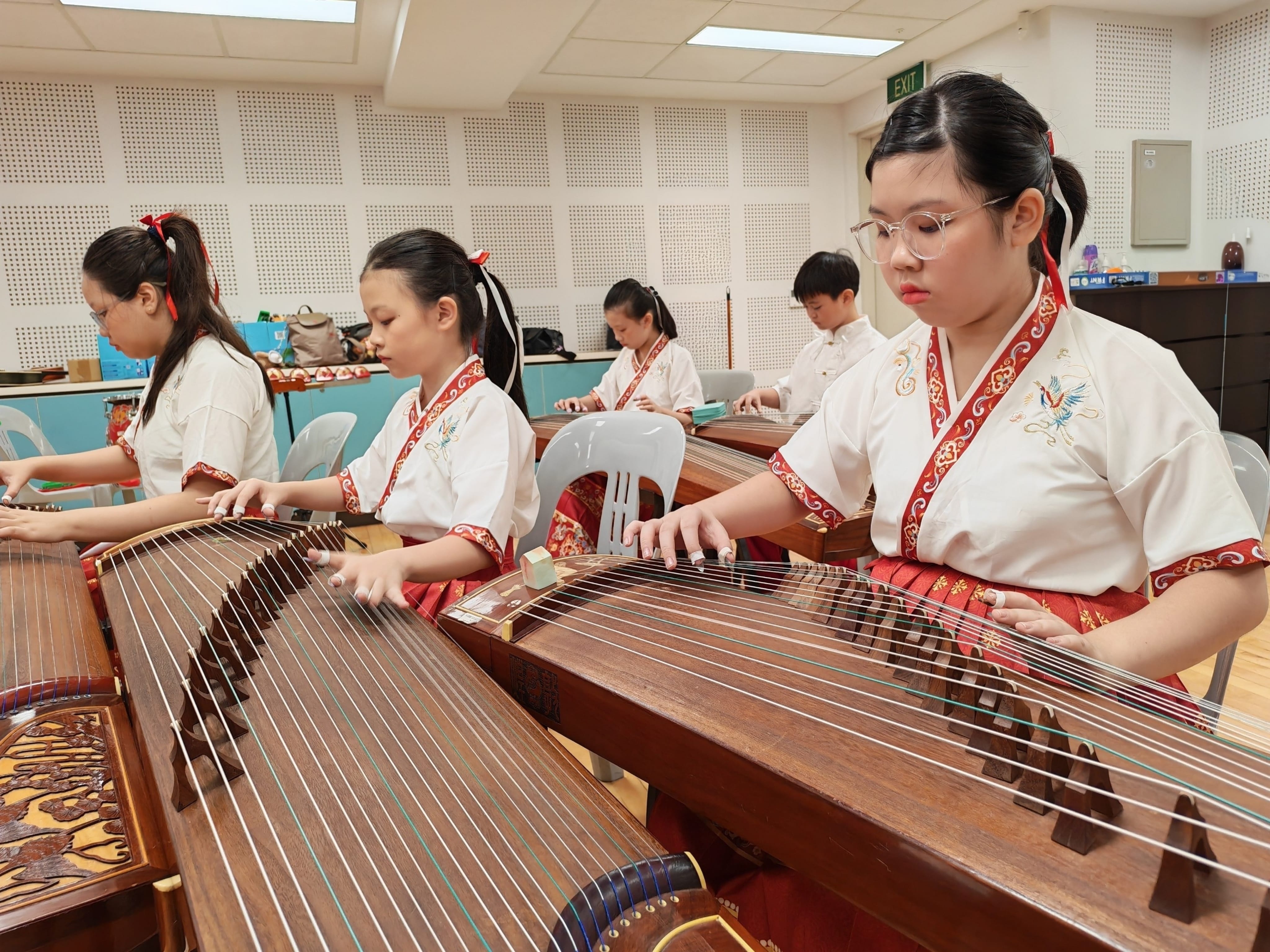 Students in performing uniforms practice playing guzheng instruments